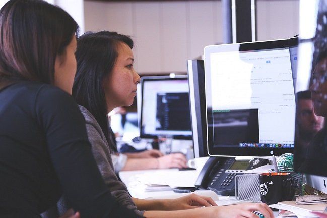 A group of people are sitting at desks in front of computer monitors.