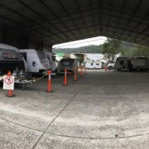 A row of rvs parked under a roof in a parking lot.