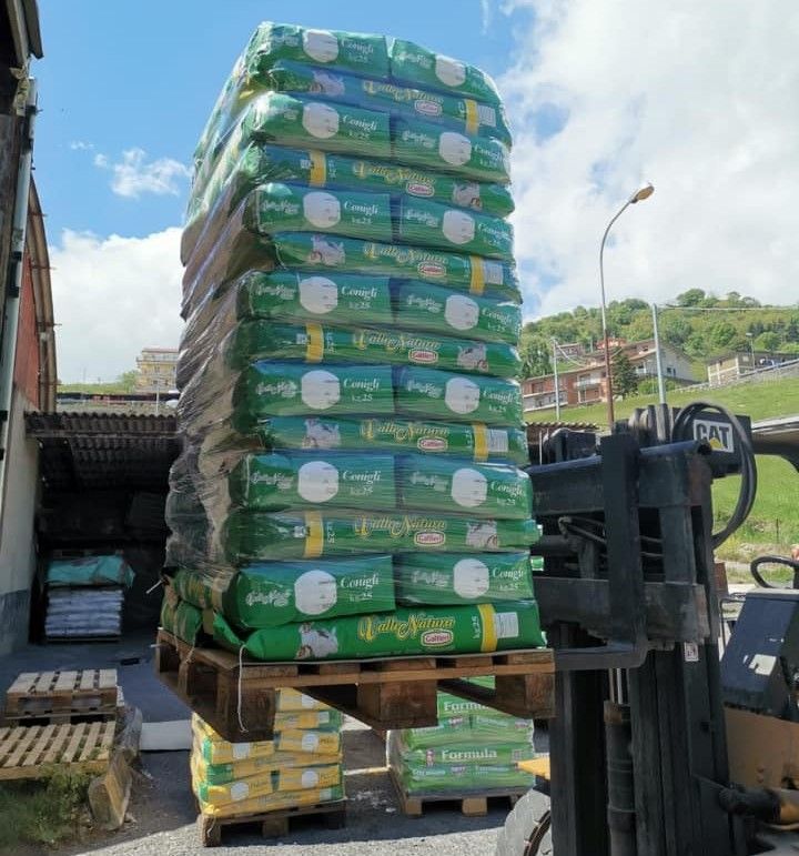 All'aperto, sotto un cielo azzurro, un carrello elevatore solleva un alto pallet di sacchi verdi di fertilizzante impilati.