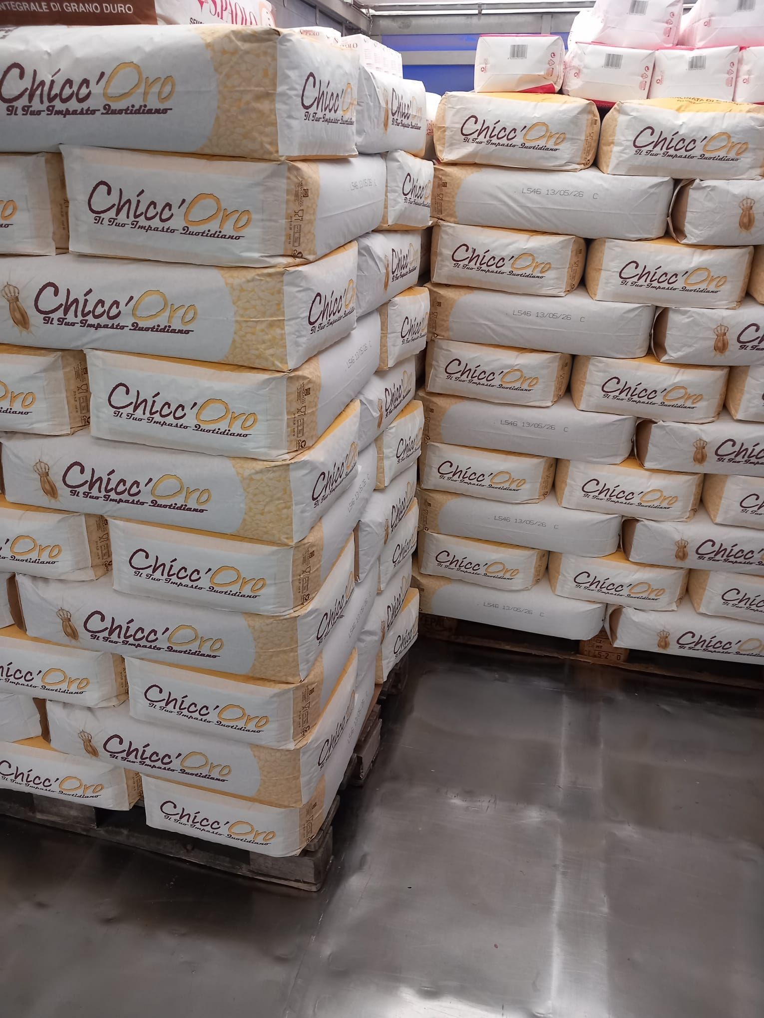 Un camion della Puglisi Cereali viene caricato con pallet di sacchi di grano, mentre in primo piano si vede un carrello elevatore che ne trasporta una pila.