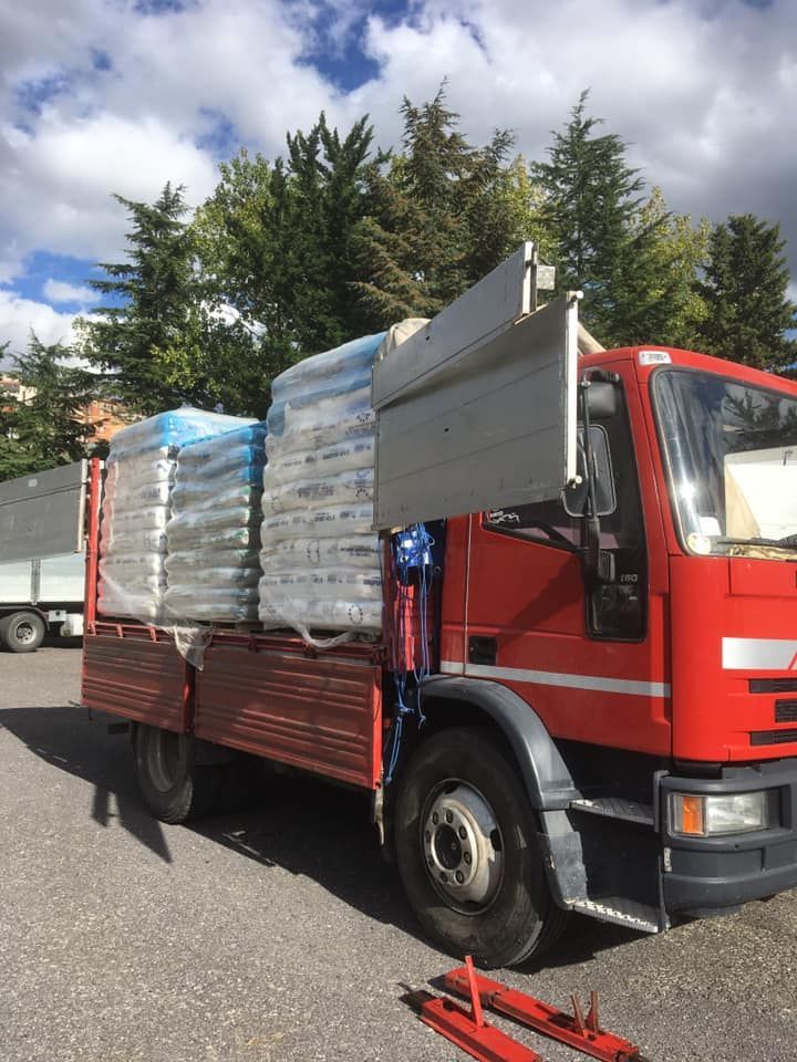 Un camioncino rosso a pianale ribassato parcheggiato all'aperto, carico di due grandi pallet di sacchi bianchi avvolti in pellicola termoretraibile.
