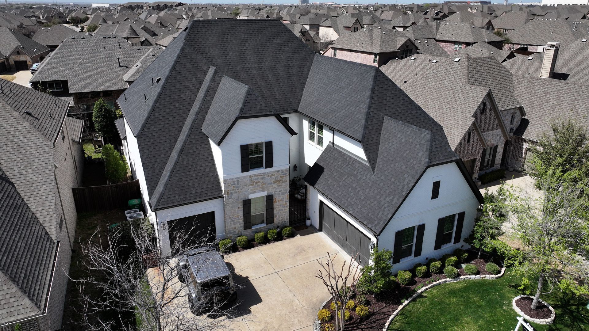 A white, two-story suburban home with a dark shingled roof, a stone facade, and a driveway with a parked car.