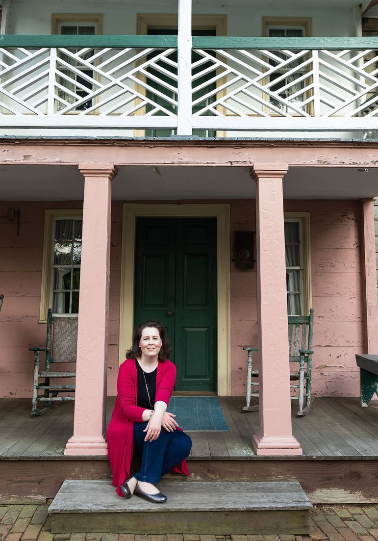 Woman in red sweater, jeans sits on porch. Primer & Scout, LLC welcomes solopreneurs, small business owners.