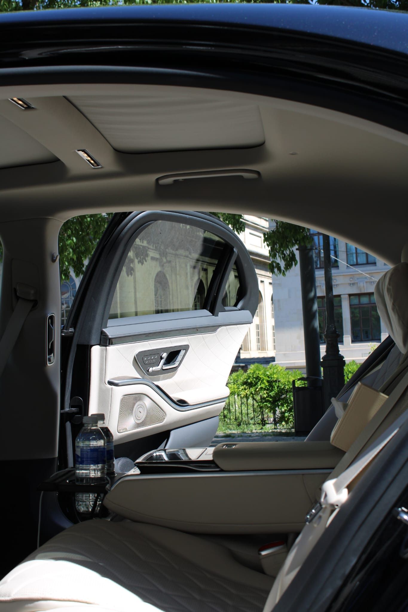 Intérieur d'une voiture avec porte arrière ouverte montrant un SUV blanc garé à l'extérieur en plein jour