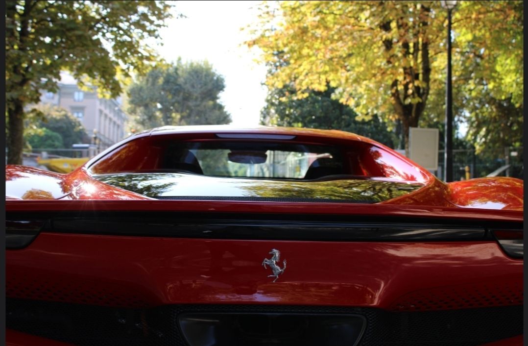 Voiture de sport rouge vue de l'arrière dans une rue bordée d'arbres, en plein jour.