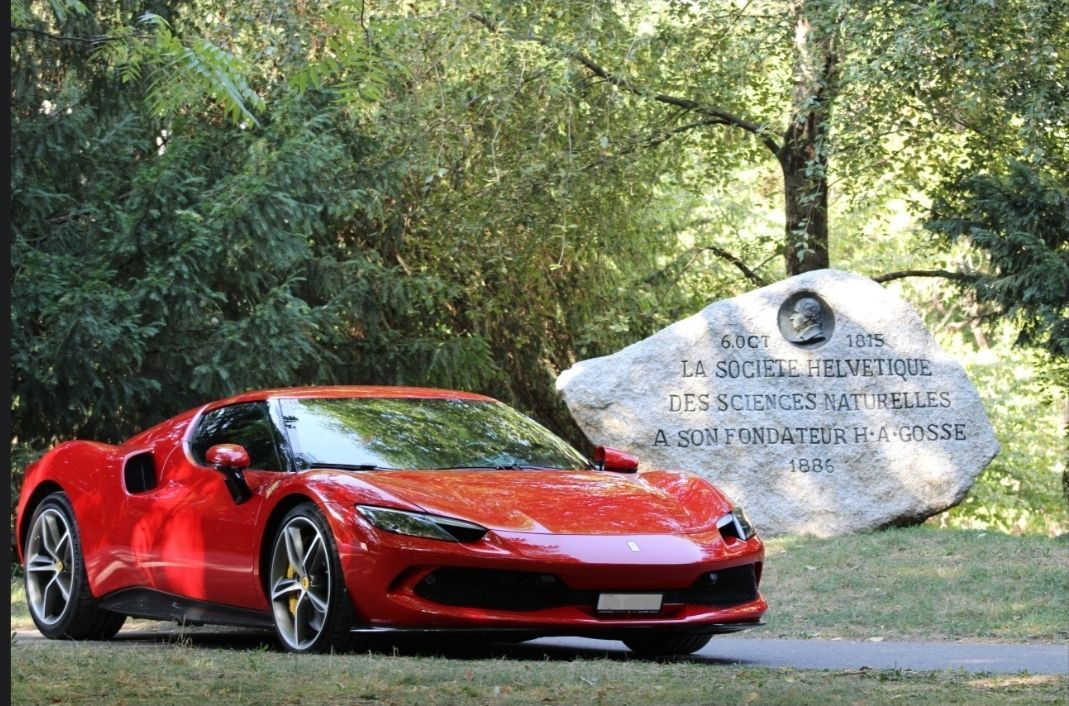 Voiture de sport rouge garée près d'un panneau en pierre dans une zone boisée
