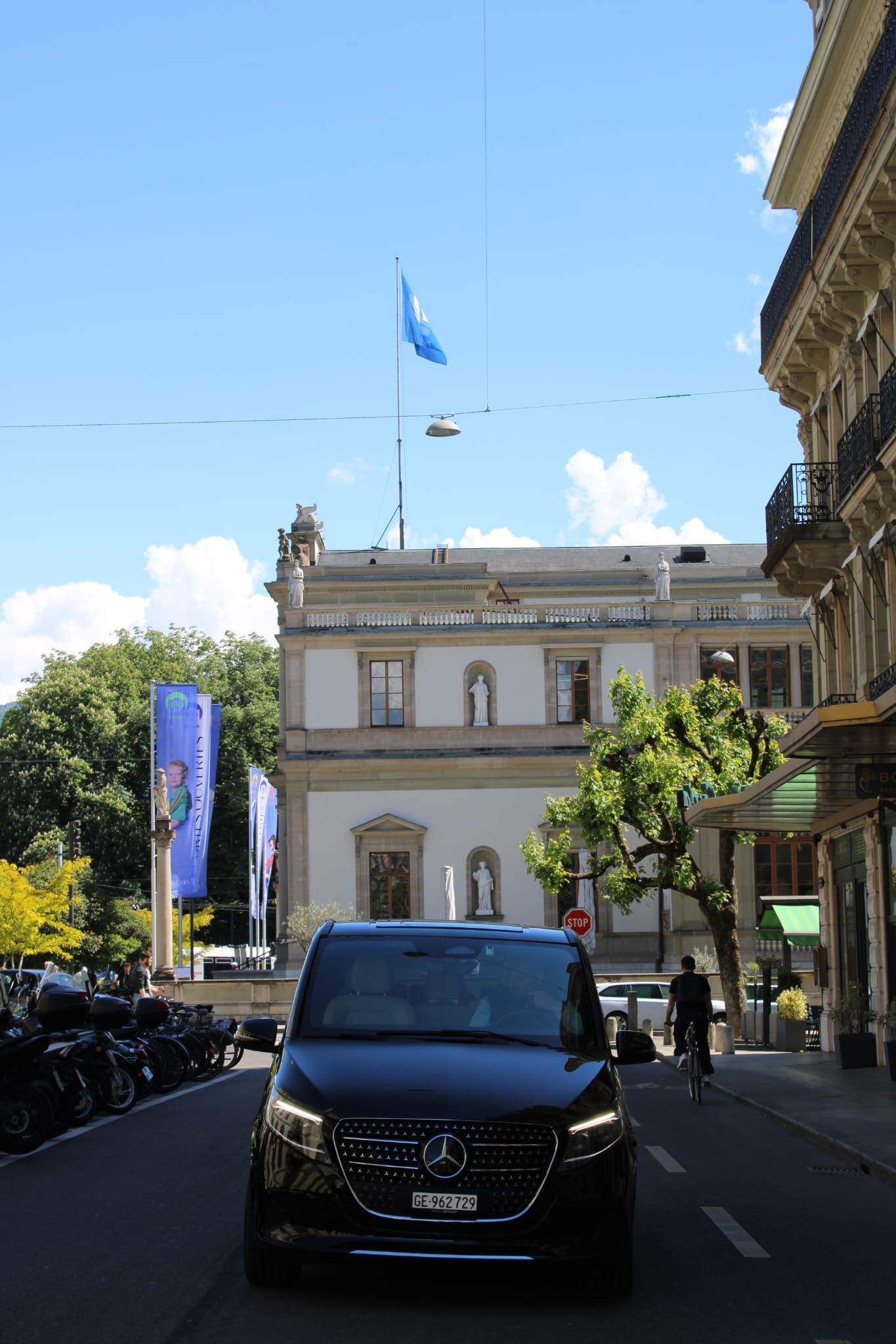 Rue avec une camionnette noire devant un bâtiment néoclassique blanc sous un ciel bleu.