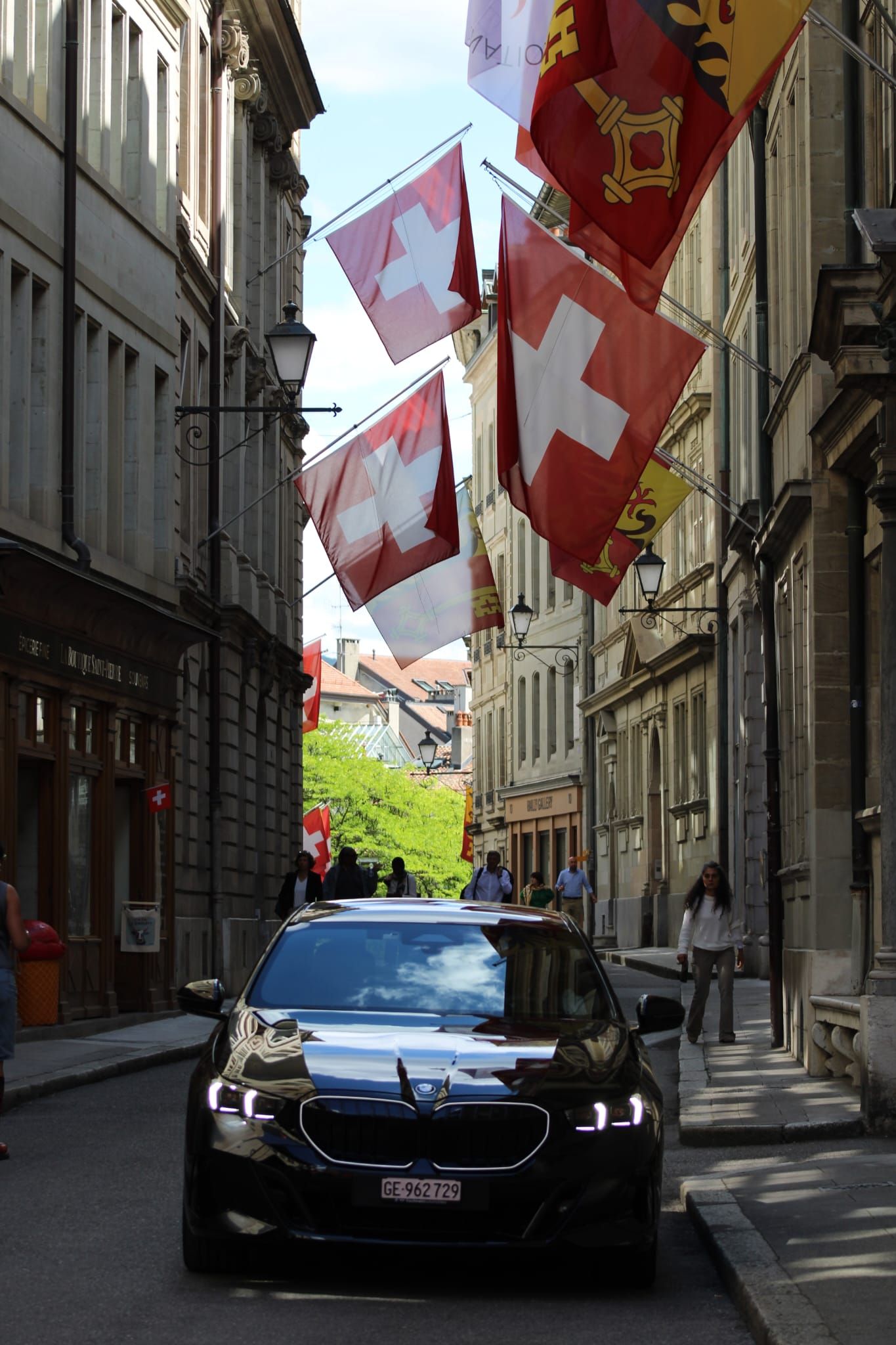 Voiture noire dans une rue étroite de la ville, des drapeaux suisses flottant entre les hauts immeubles.