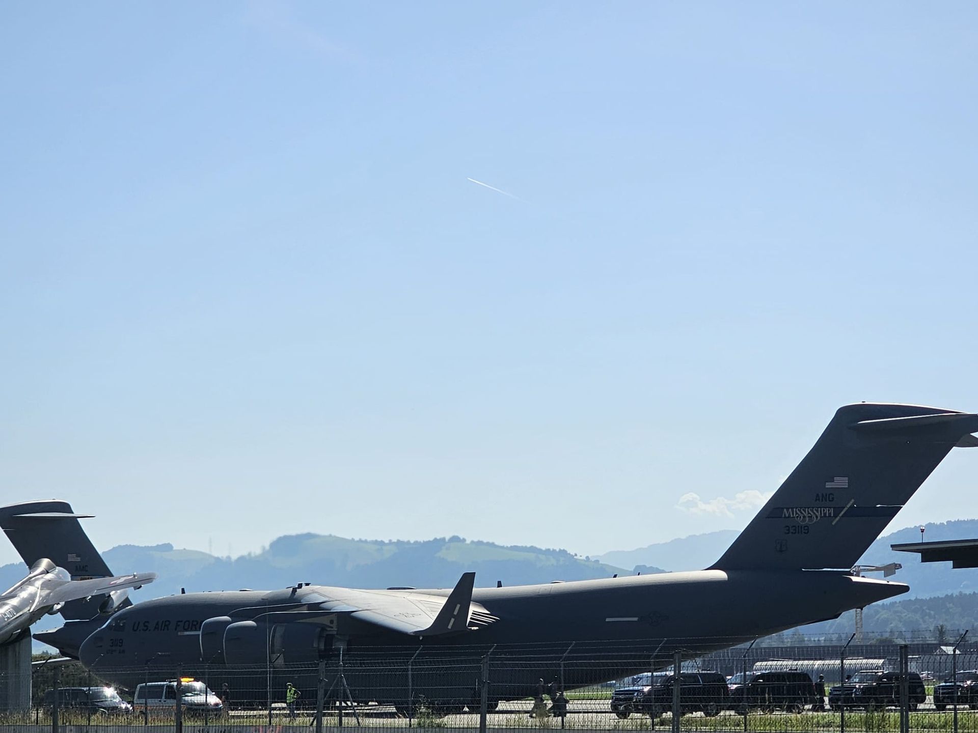 Avion cargo militaire stationné sur une piste sous un ciel bleu dégagé, avec des montagnes en arrière-plan.