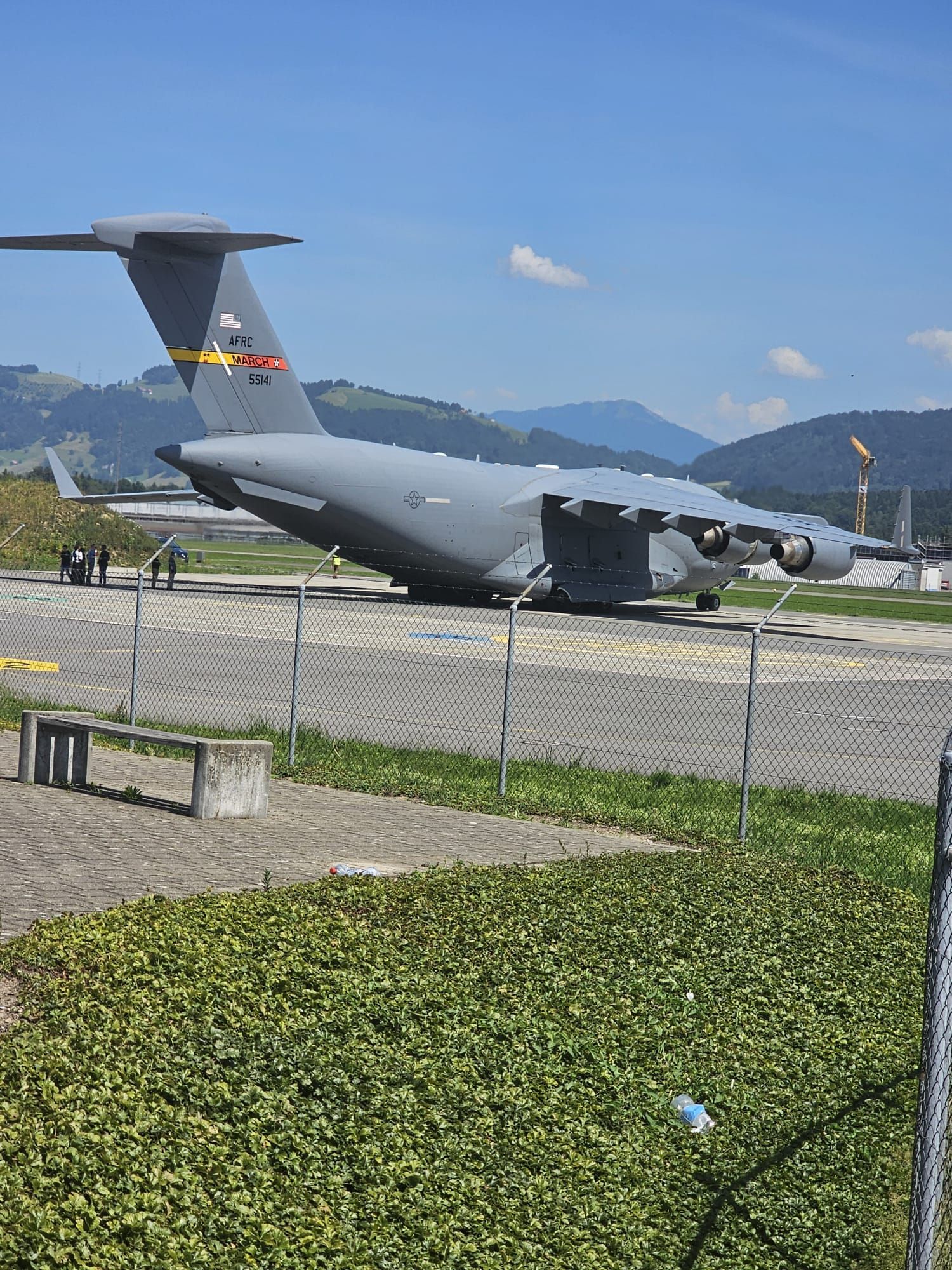 Un avion cargo militaire gris est exposé derrière une clôture dans un musée en plein air, avec des montagnes en arrière-plan.