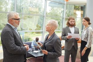 A group of business people are standing in a room talking to each other.