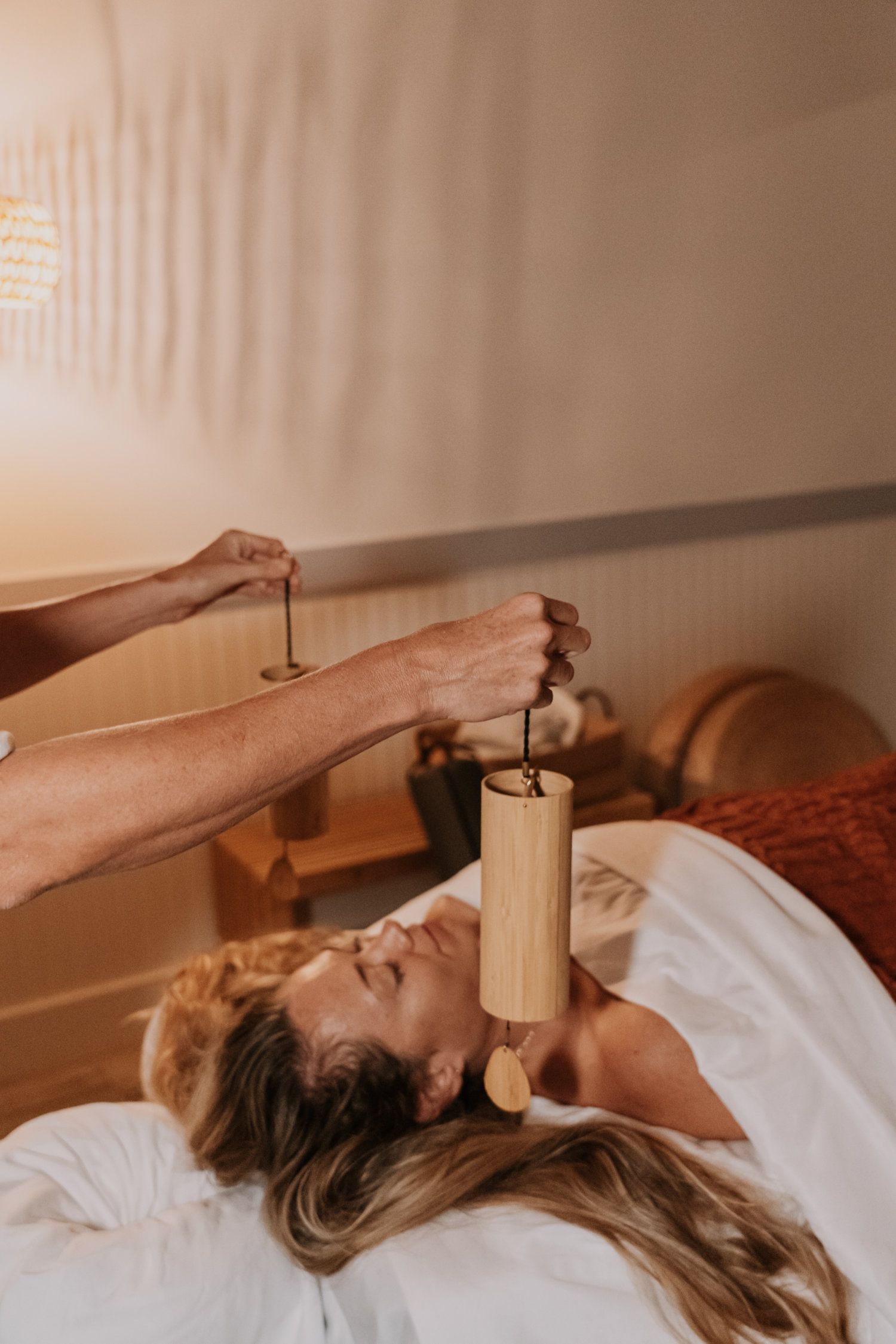 Person receiving sound therapy with wooden chimes, lying on a massage table in a warm room.