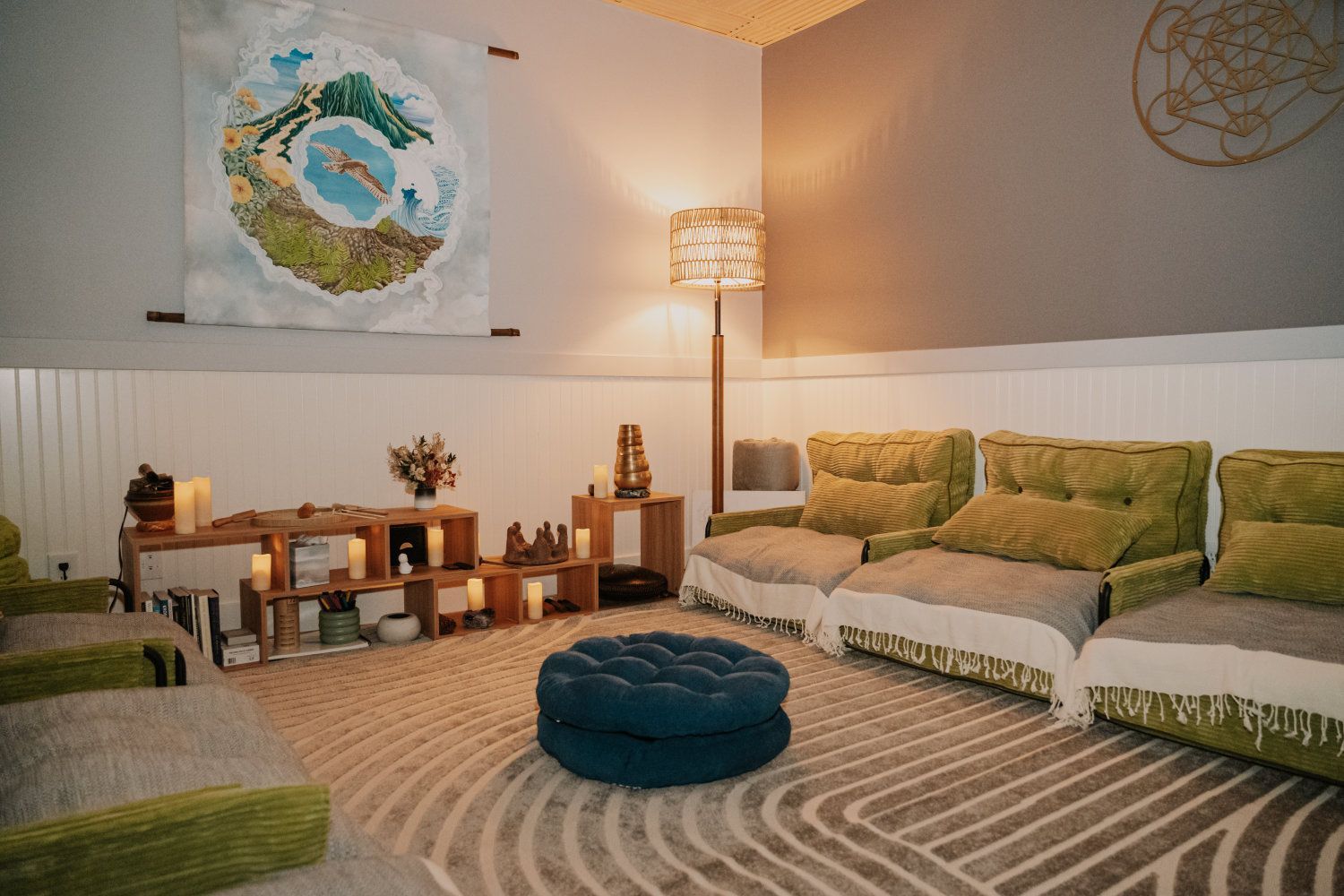 Relaxation room with green seating, a blue ottoman, and a decorative tapestry.