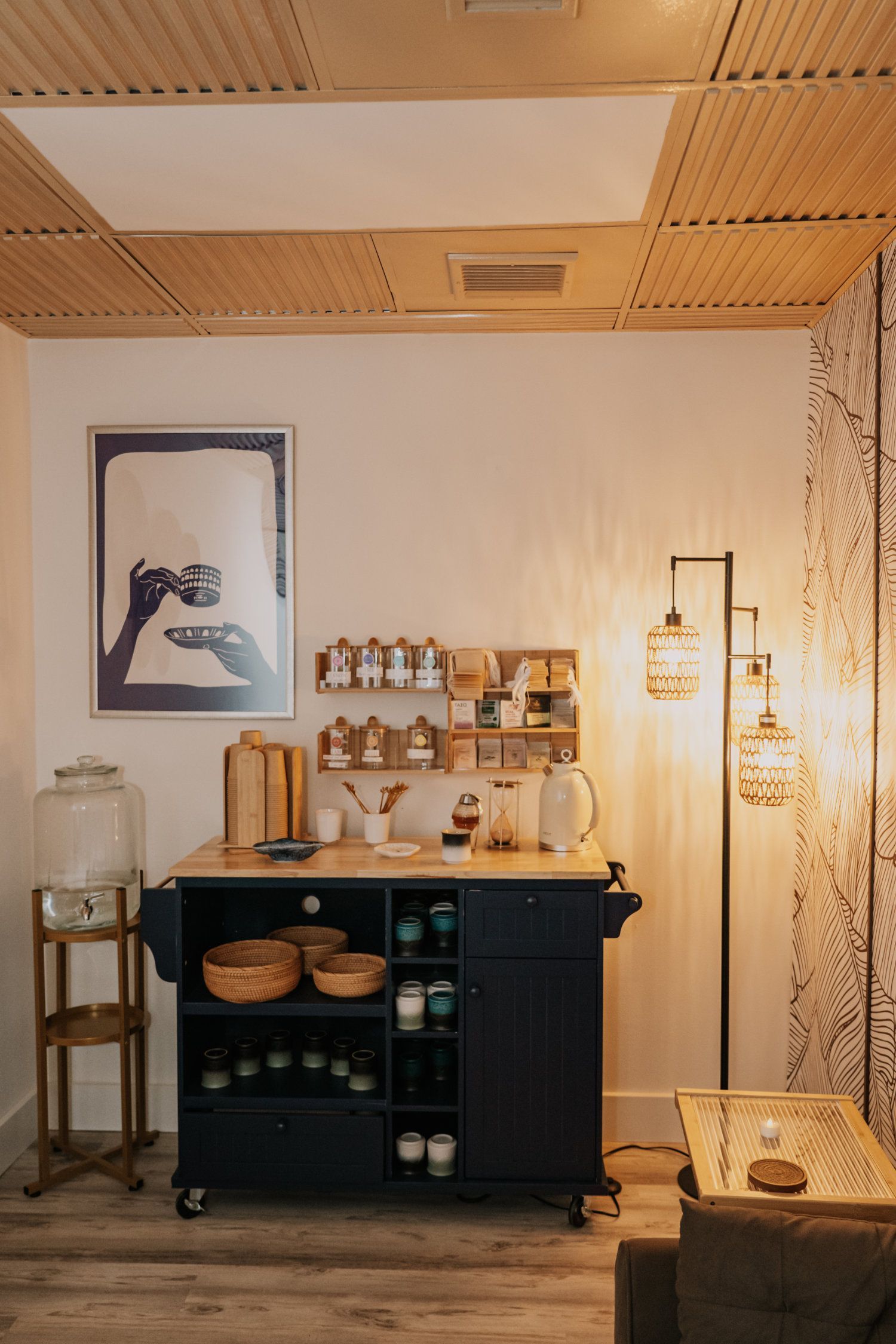 Kitchen cart with spices, art, and water dispenser in a bright room with wooden ceiling.