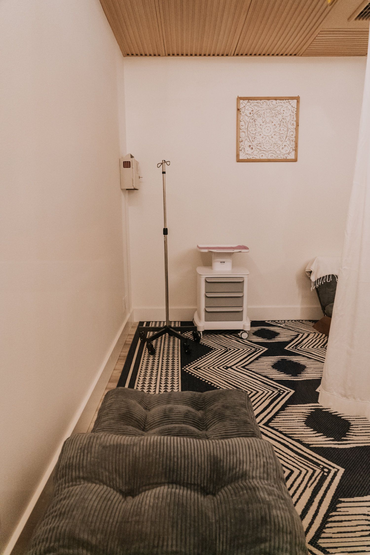 Cozy room with grey chaise lounge, patterned rug, side table, and floral arrangement. Microphone stand. Wooden ceiling.