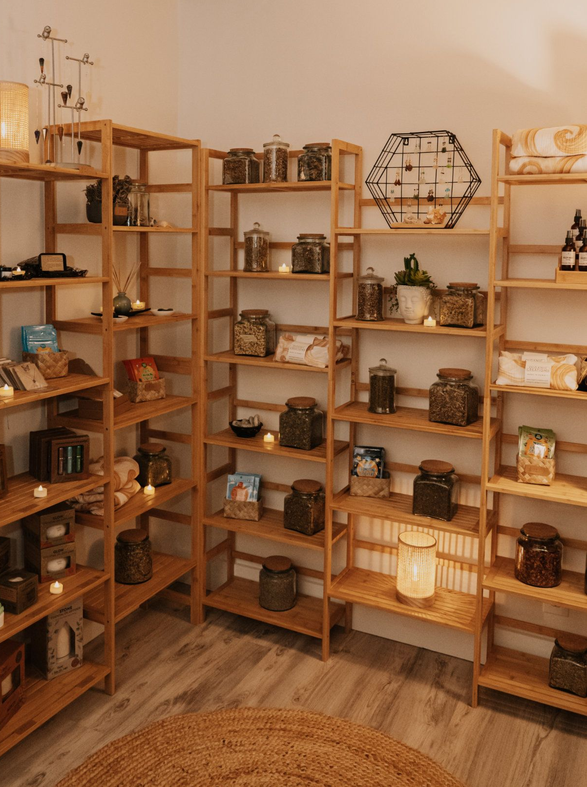 Wooden shelves displaying jars of herbs, candles, and decor. Cozy retail space with a jute rug.