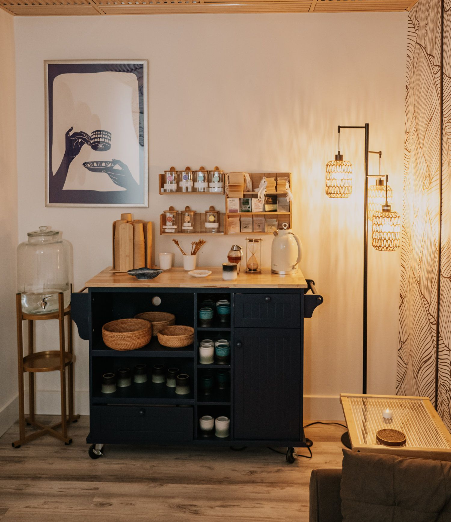 A modern kitchen cart with supplies, art, and a lamp in a warm-lit space.