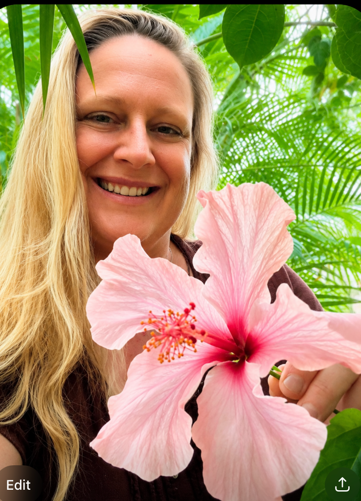 Blonde woman smiling, wearing a white shirt, in a garden setting.