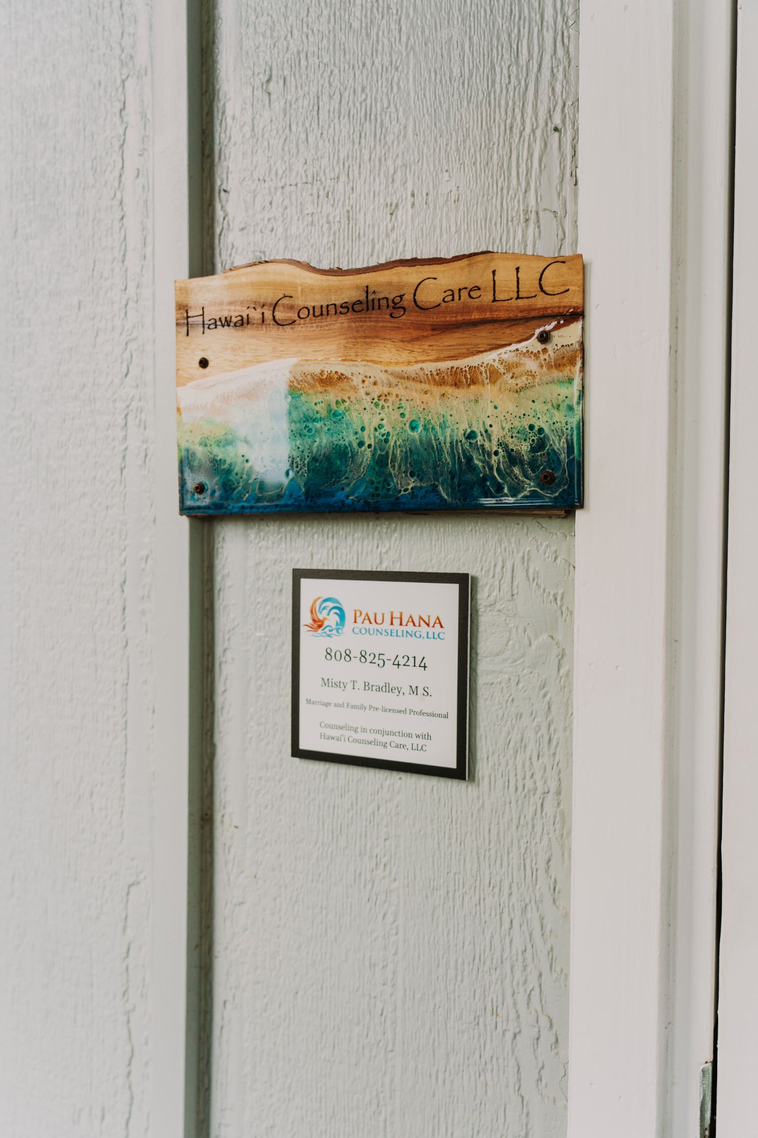 Sign on weathered white wall, featuring a beach scene and a business notice.