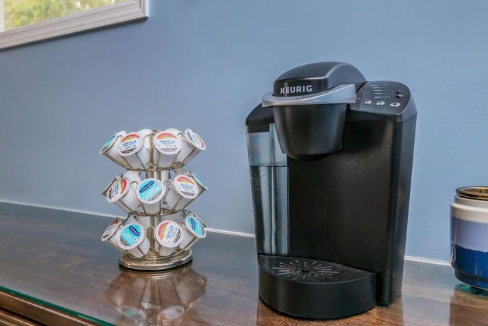 Black Keurig coffee maker with a K-cup carousel on a counter. Blue wall in the background.