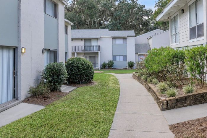 Apartment complex with walkways, grass, and shrubbery. Buildings are white with some blue-gray accents.