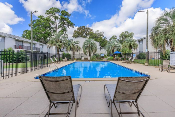 Two lounge chairs face a rectangular pool at an apartment complex on a sunny day.