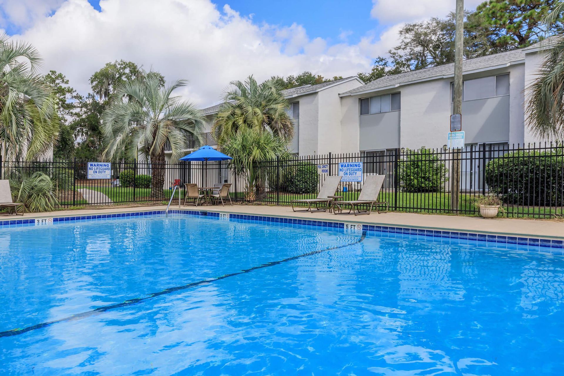 Swimming pool with blue water, chairs, umbrella, and building in the background.
