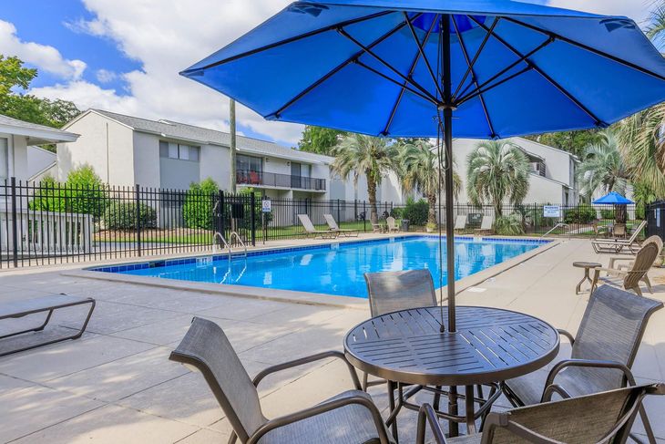 Swimming pool with a blue umbrella, table, chairs, and apartment buildings.