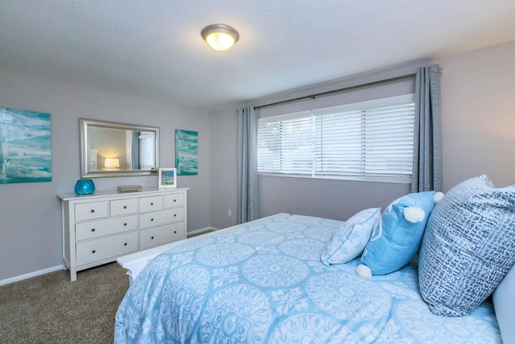 Bedroom with a bed, dresser, and blue accents. Light blue comforter, gray walls, and window with blinds.