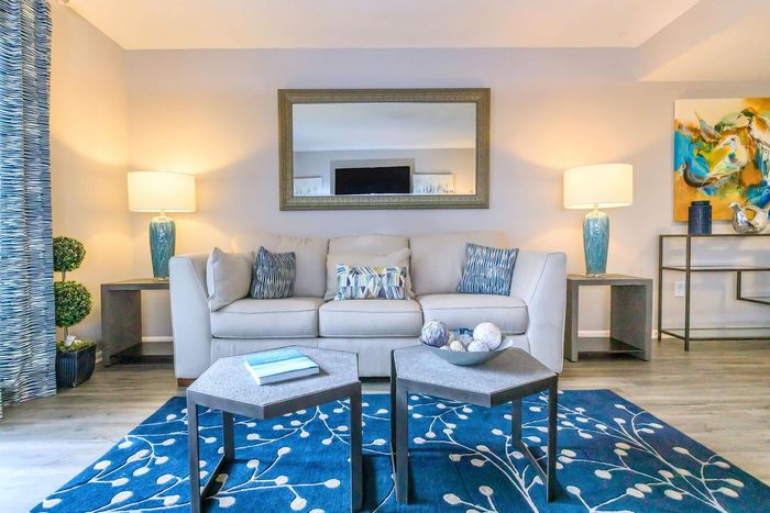 Living room with beige sofa, blue rug, artwork, and lamps.