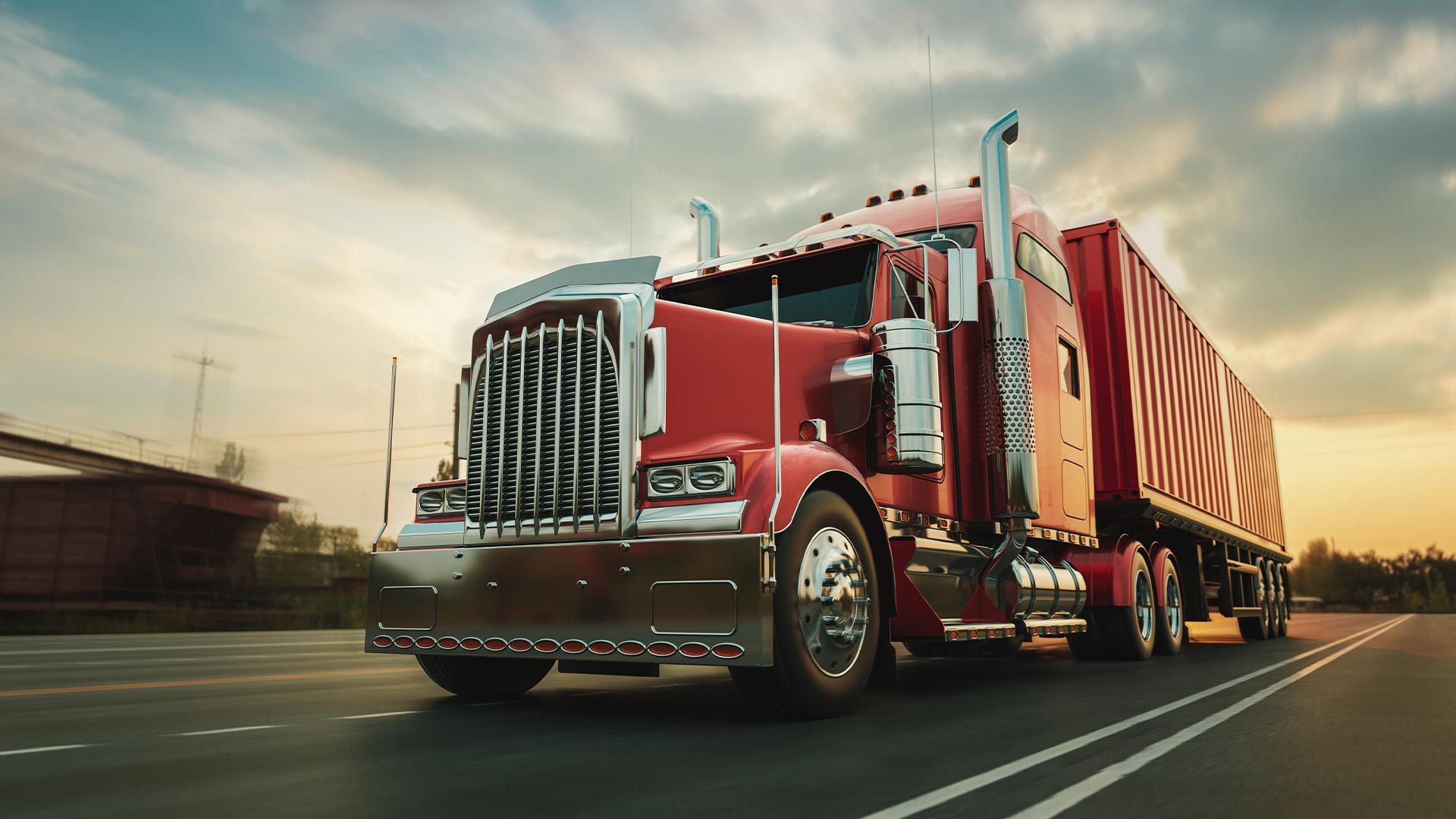 Red semi-truck driving on a road under a sunset sky.