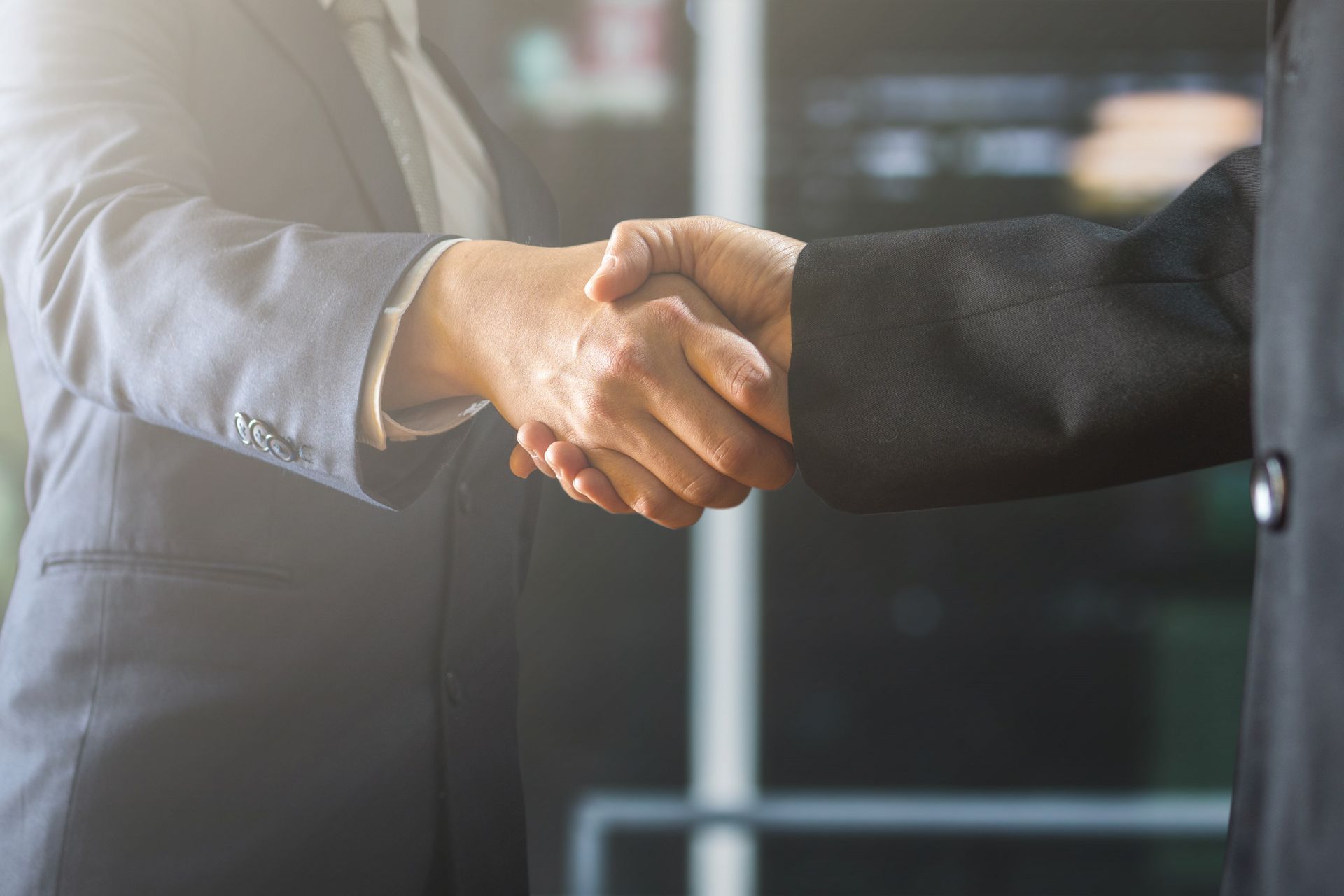 Two businesspeople shake hands, likely closing a deal, indoors.