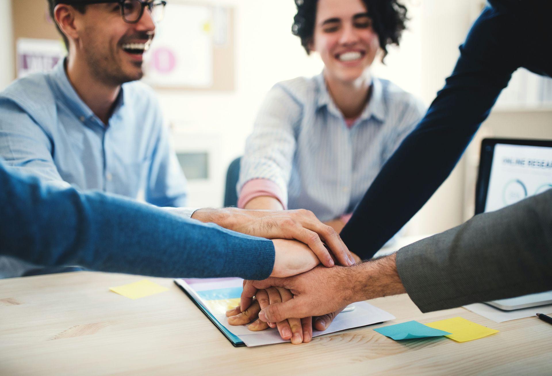 Team of people with hands stacked together, smiling and celebrating success at a desk.