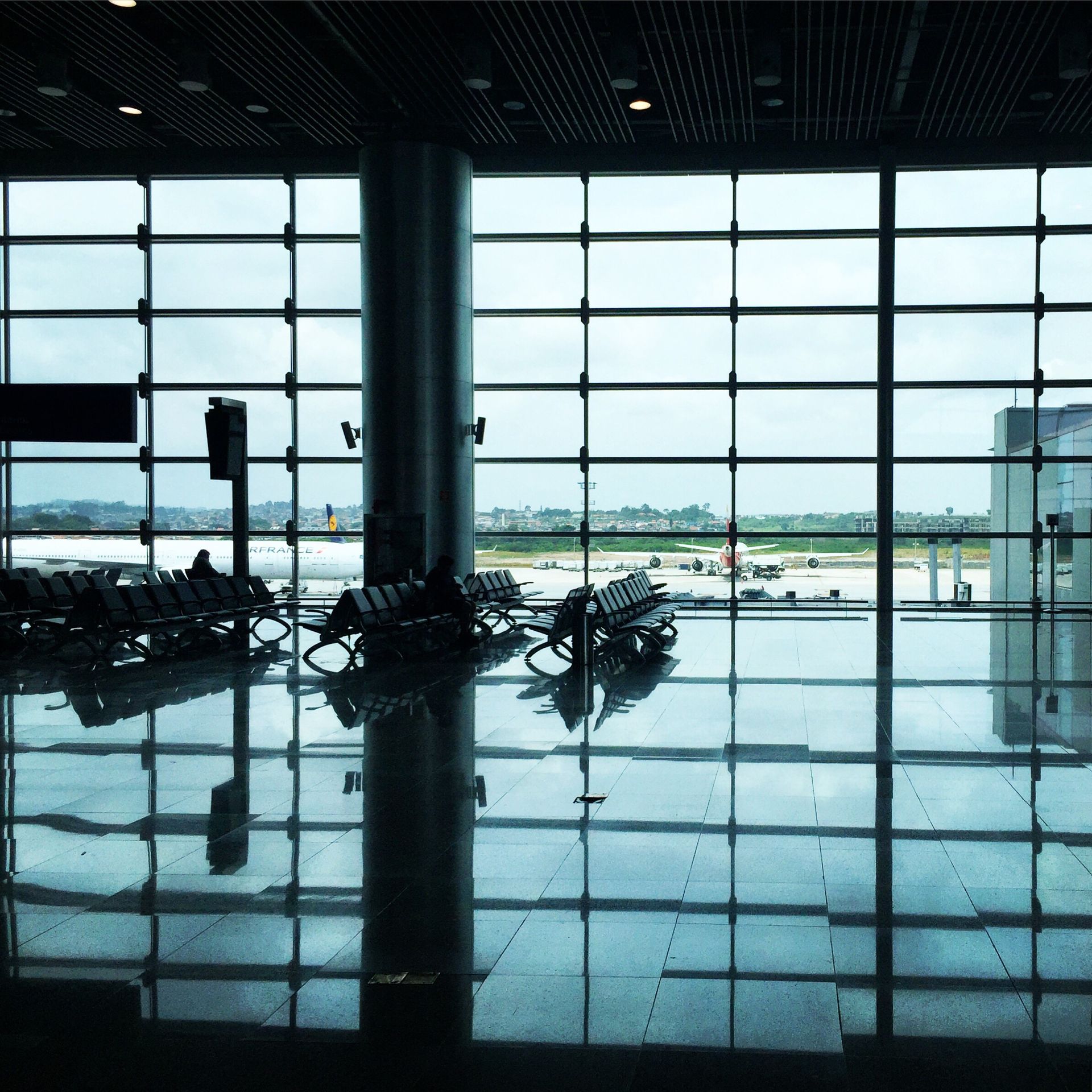Inside an airport terminal with a reflective floor, looking out at the tarmac and a cloudy sky.