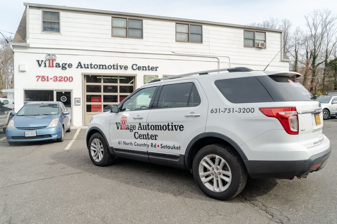 Village Automotive Center, white SUV parked outside garage. Business name on vehicle and building, phone number visible.