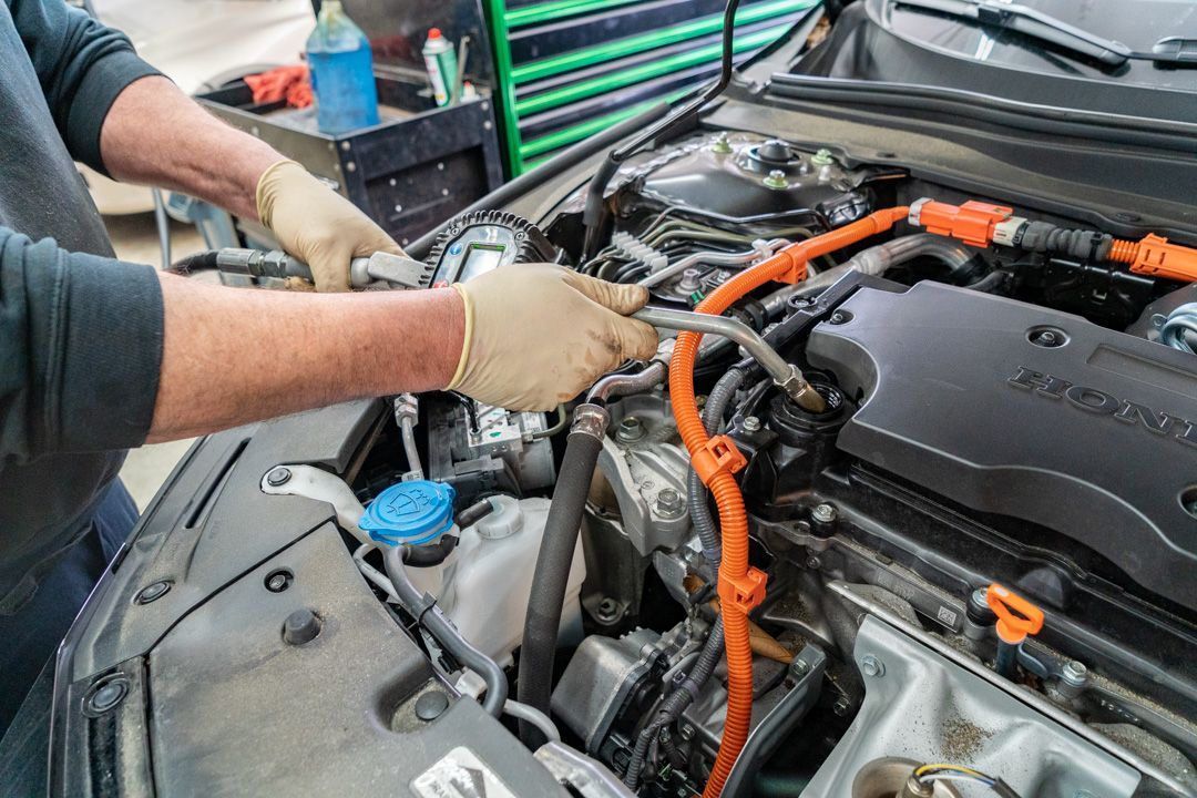 Mechanic working on car engine, using a wrench. Hands wear gloves. Orange cable visible.