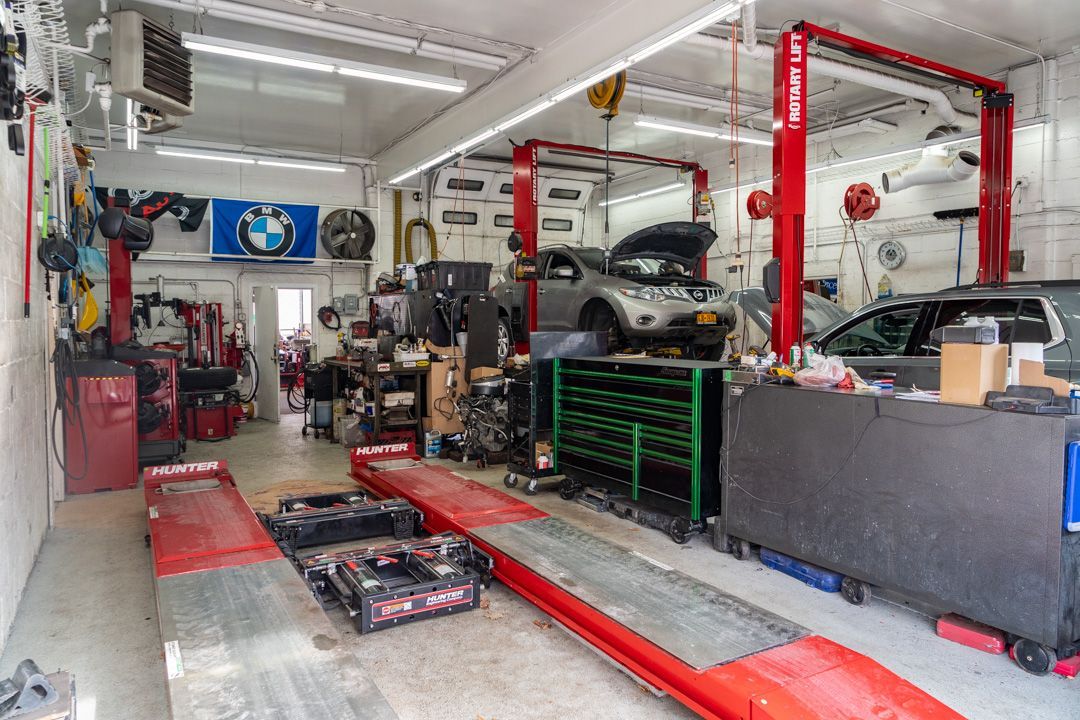 Car repair shop interior with vehicle on lift, tools, and equipment. Red, gray, and white dominate the space.
