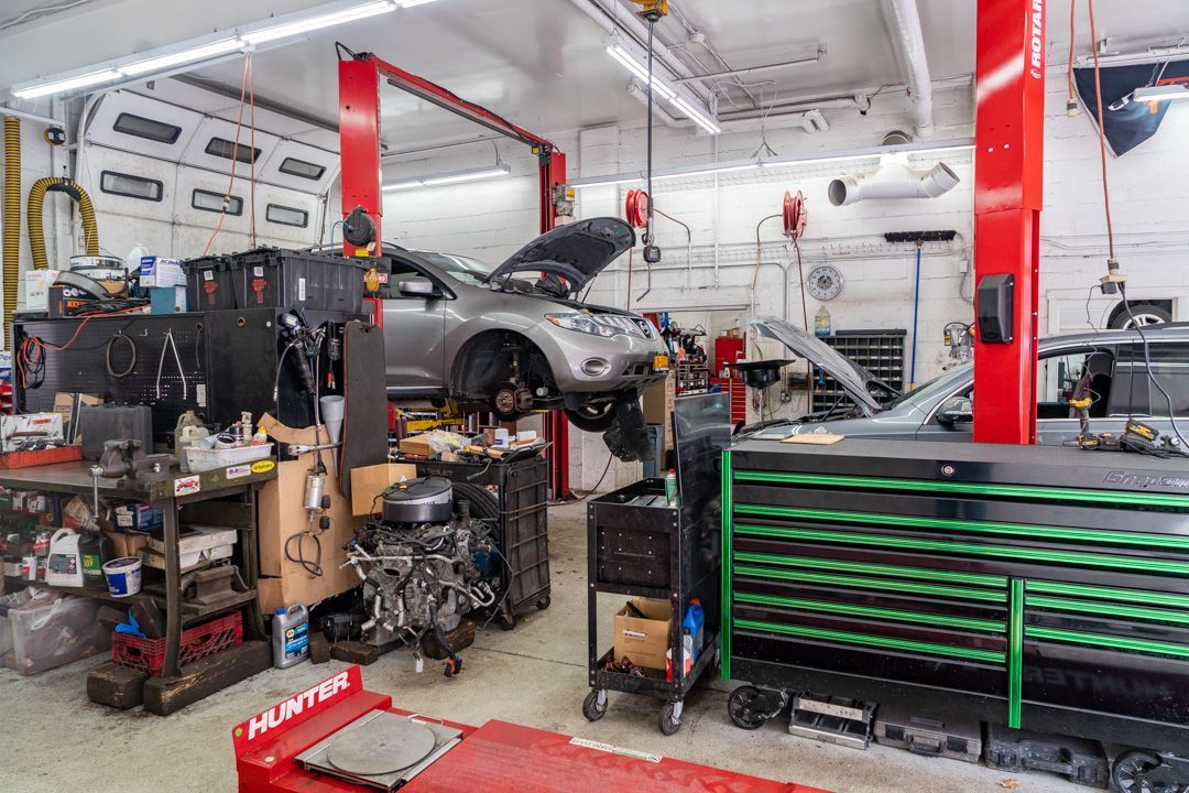 A car is lifted in a garage, open hood, tools, and a toolbox. Red support columns, work environment.