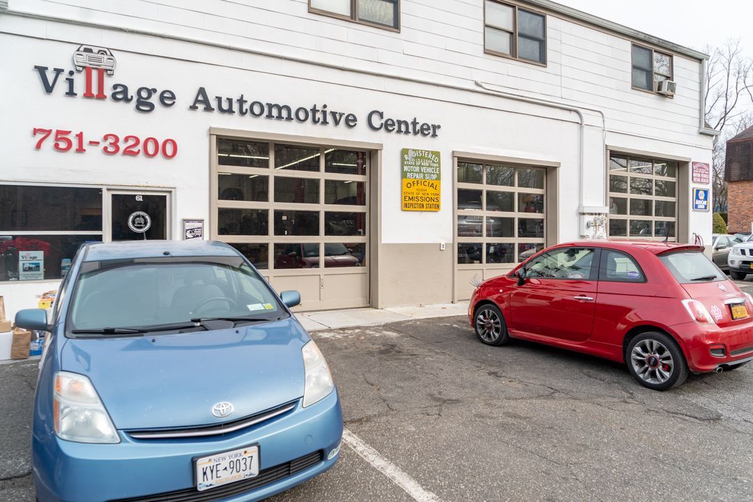 Exterior of Village Automotive Center with a blue Prius and red Fiat 500 parked outside.