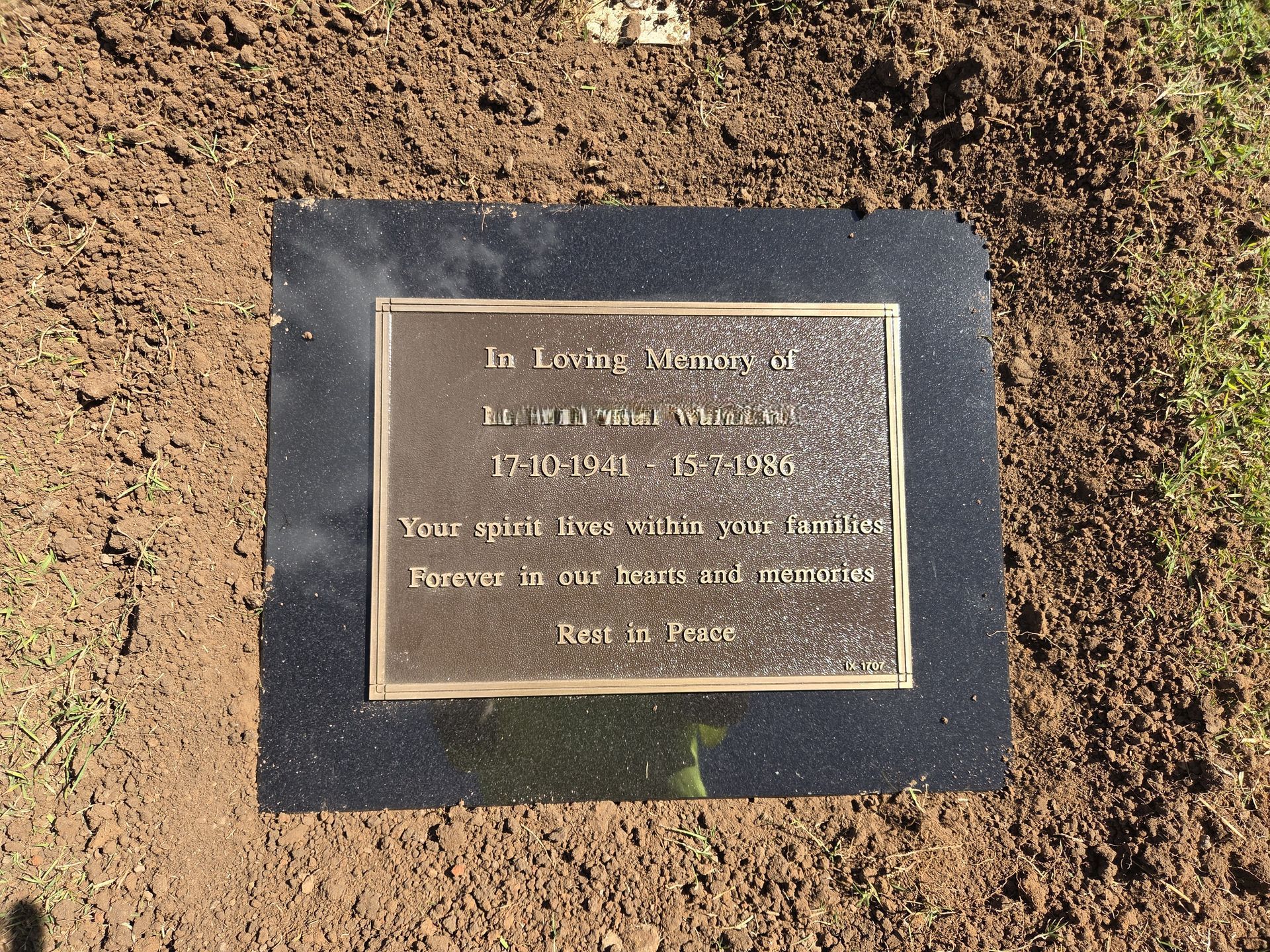 Bronze memorial plaque with engraved text and decorative trees, set on newspaper with blue painter's tape.