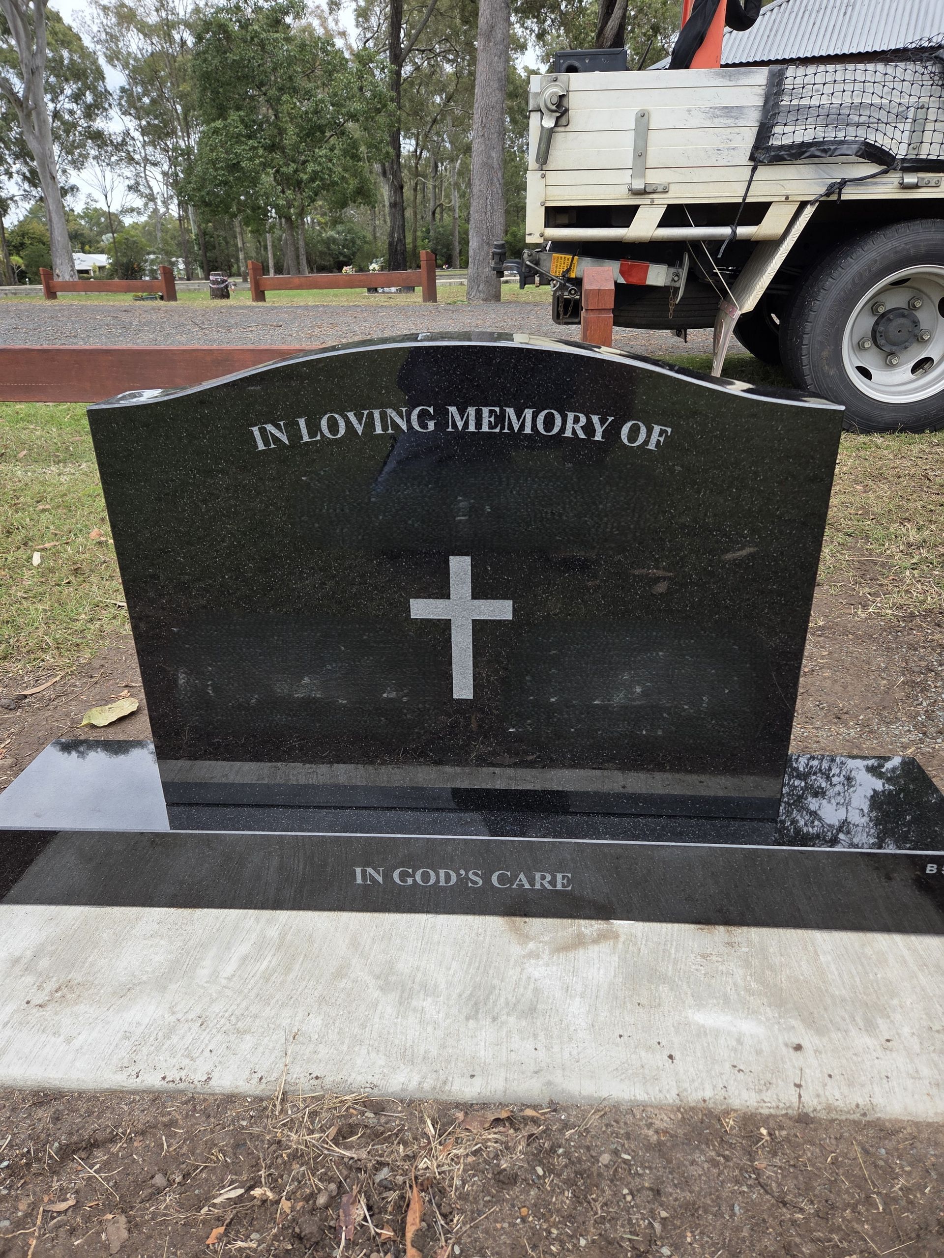 Black granite headstone with bronze plaque and flowers; in a cemetery.