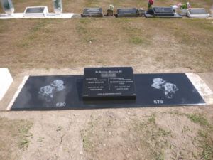 Black granite tombstone with engraved names, two dog images, and surrounding gravestones.