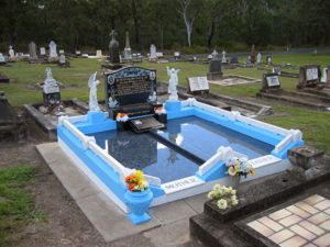 Elaborate tombstone in cemetery, blue and white trim, reflective surface, angels, flowers.