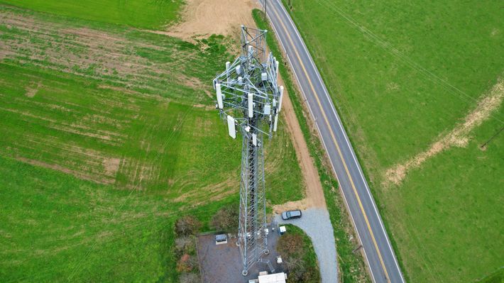 An aerial view of a cell phone tower in the middle of a field next to a road.