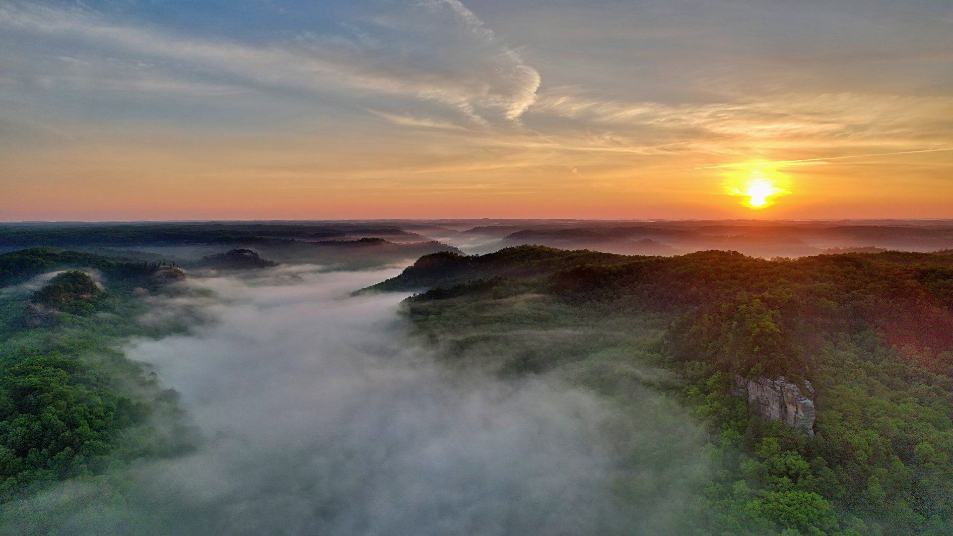 An aerial view of a foggy valley at sunset.
