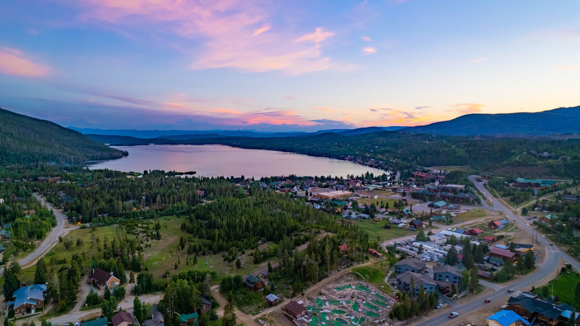 An aerial view of a lake surrounded by trees and houses at sunset.