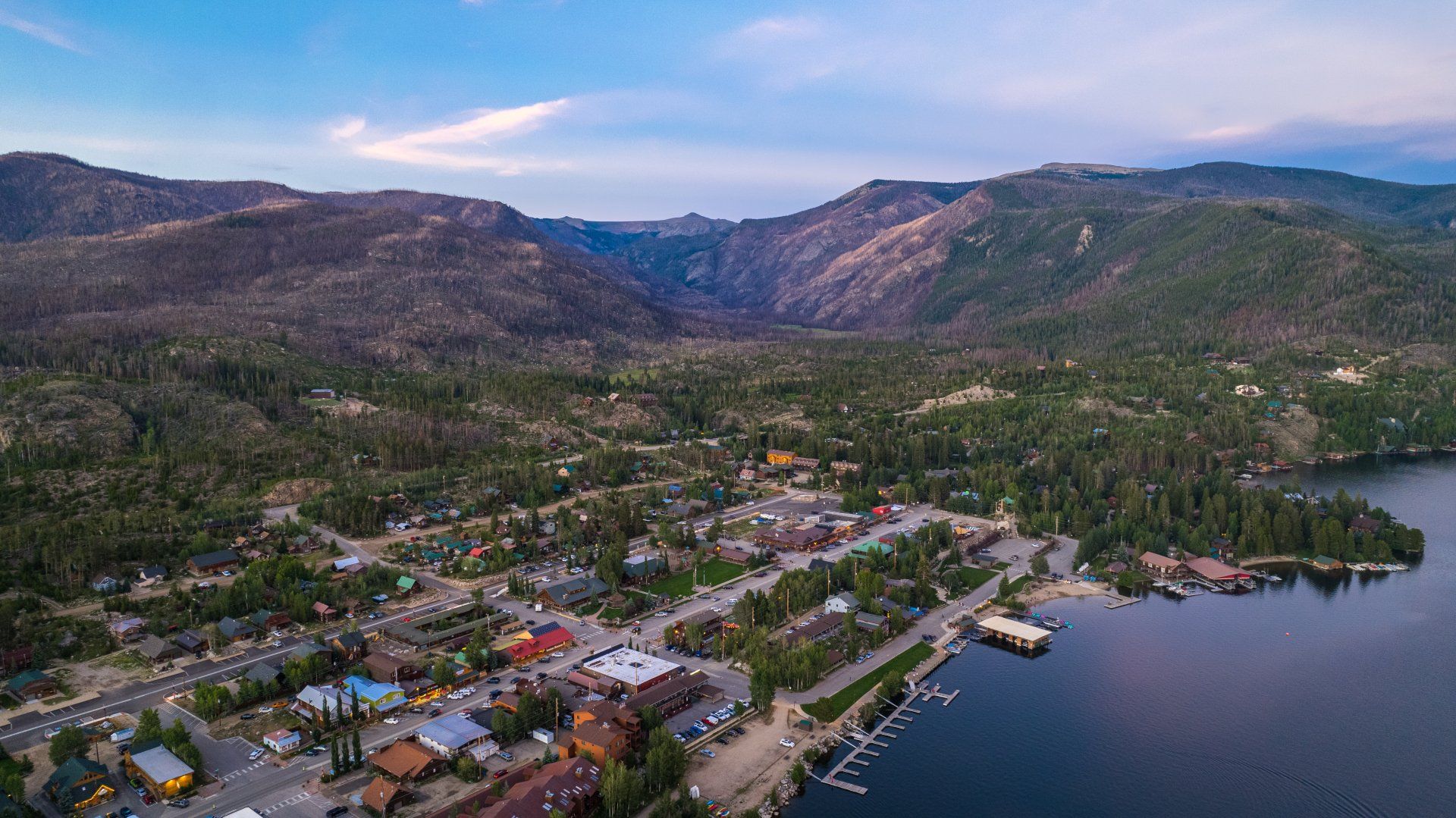 An aerial view of a small town next to a lake with mountains in the background.