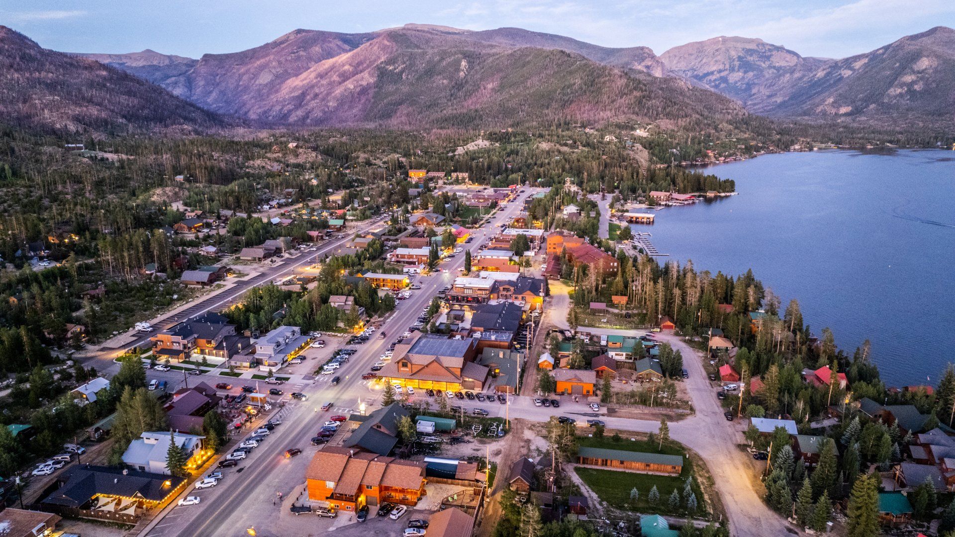 An aerial view of a small town next to a lake with mountains in the background.