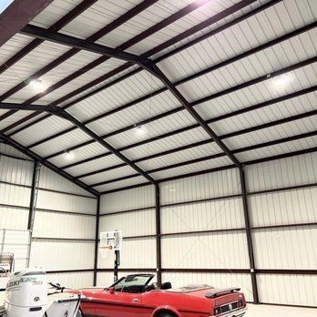 A red mustang is parked inside of a metal building.