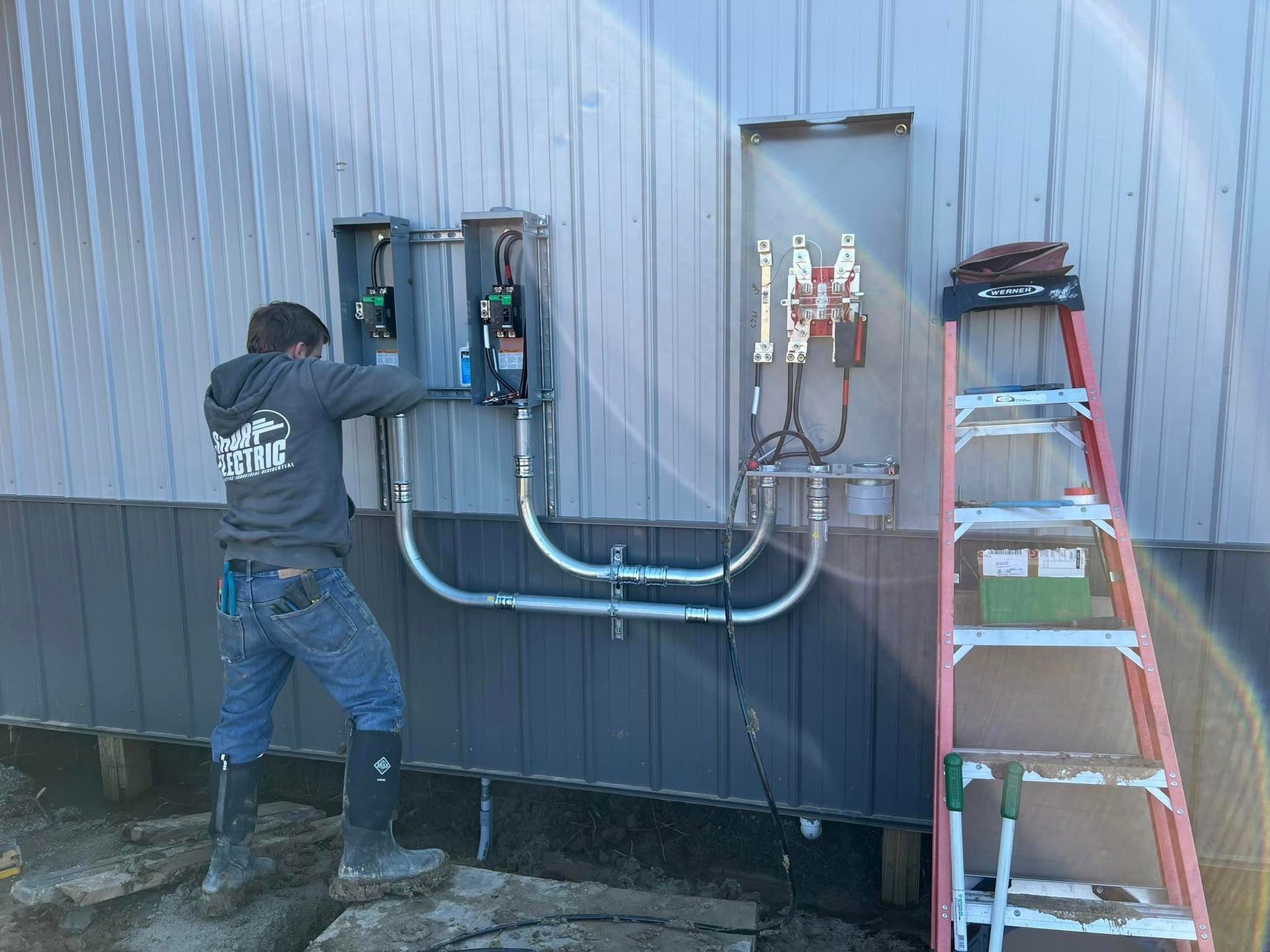 A man is working on an electrical box on the side of a building next to a ladder.